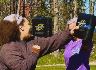 A participant practices a punch into a padded target held by an instructor during an outdoor self-defense training.